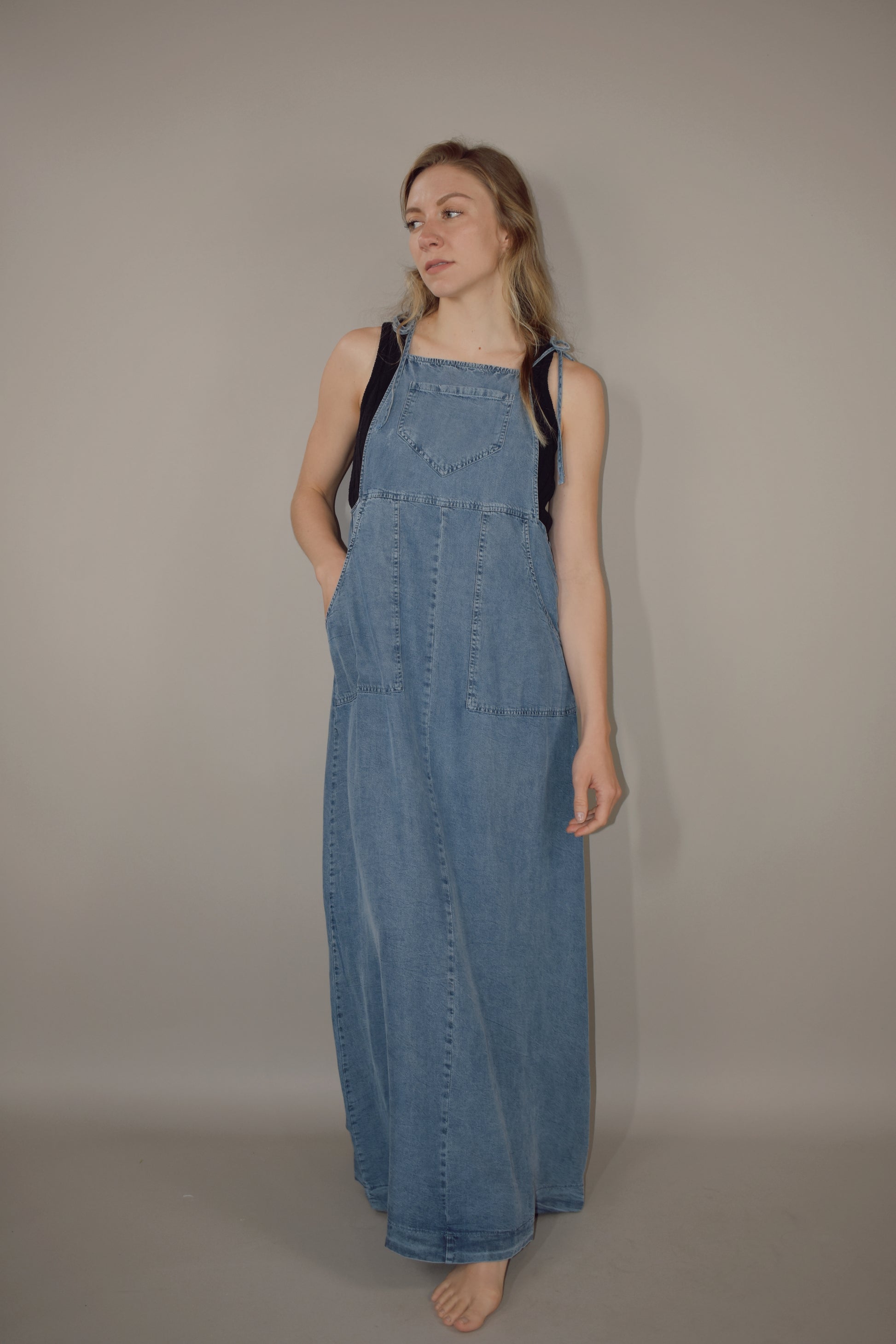 soft and lightweight overall maxi dress with front pocket on bodice and two long patch pockets on skirt. thin spaghetti tie straps. medium wash denim color. flowy.