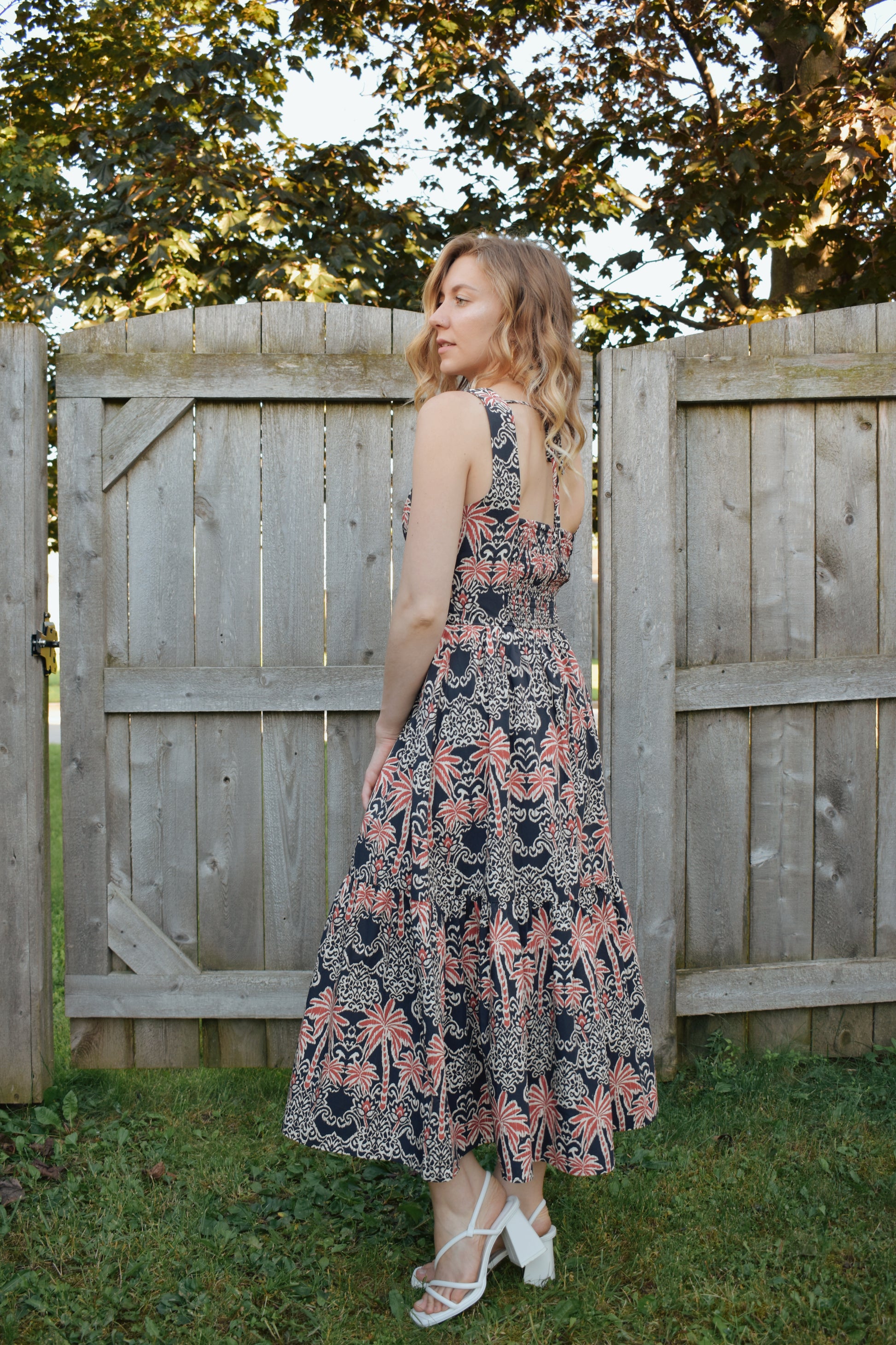 v neck midi dress with oval cut outs at waistline with circle loop in the center. square neck on back with tie across the top. sleeveless with thick tank straps. dark blue background with white and light red summer print. smocked on back waistline for stretch.