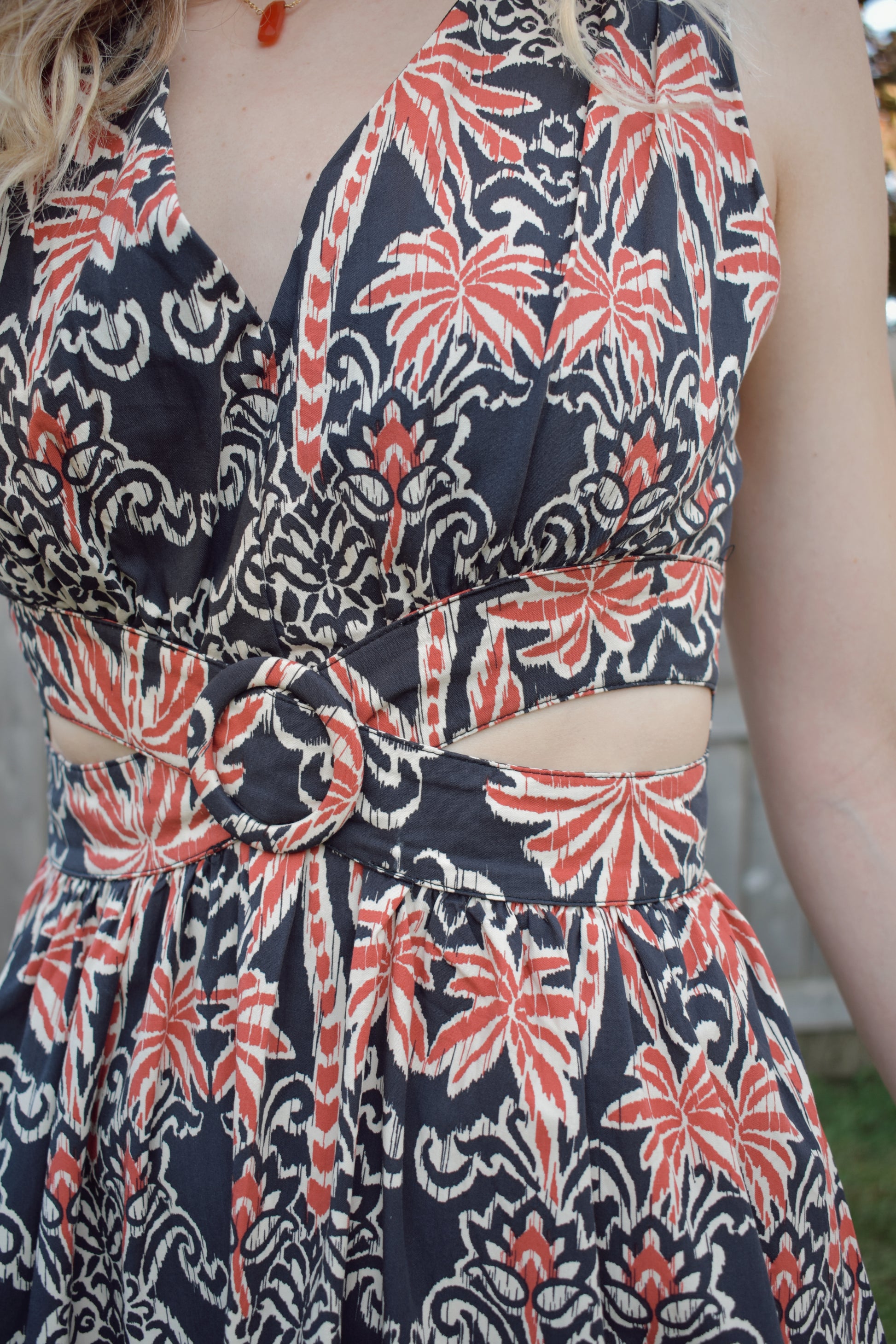 v neck midi dress with oval cut outs at waistline with circle loop in the center. square neck on back with tie across the top. sleeveless with thick tank straps. dark blue background with white and light red summer print. smocked on back waistline for stretch.