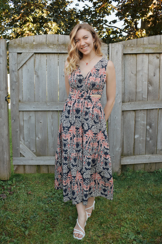 v neck midi dress with oval cut outs at waistline with circle loop in the center. square neck on back with tie across the top. sleeveless with thick tank straps. dark blue background with white and light red summer print. smocked on back waistline for stretch.