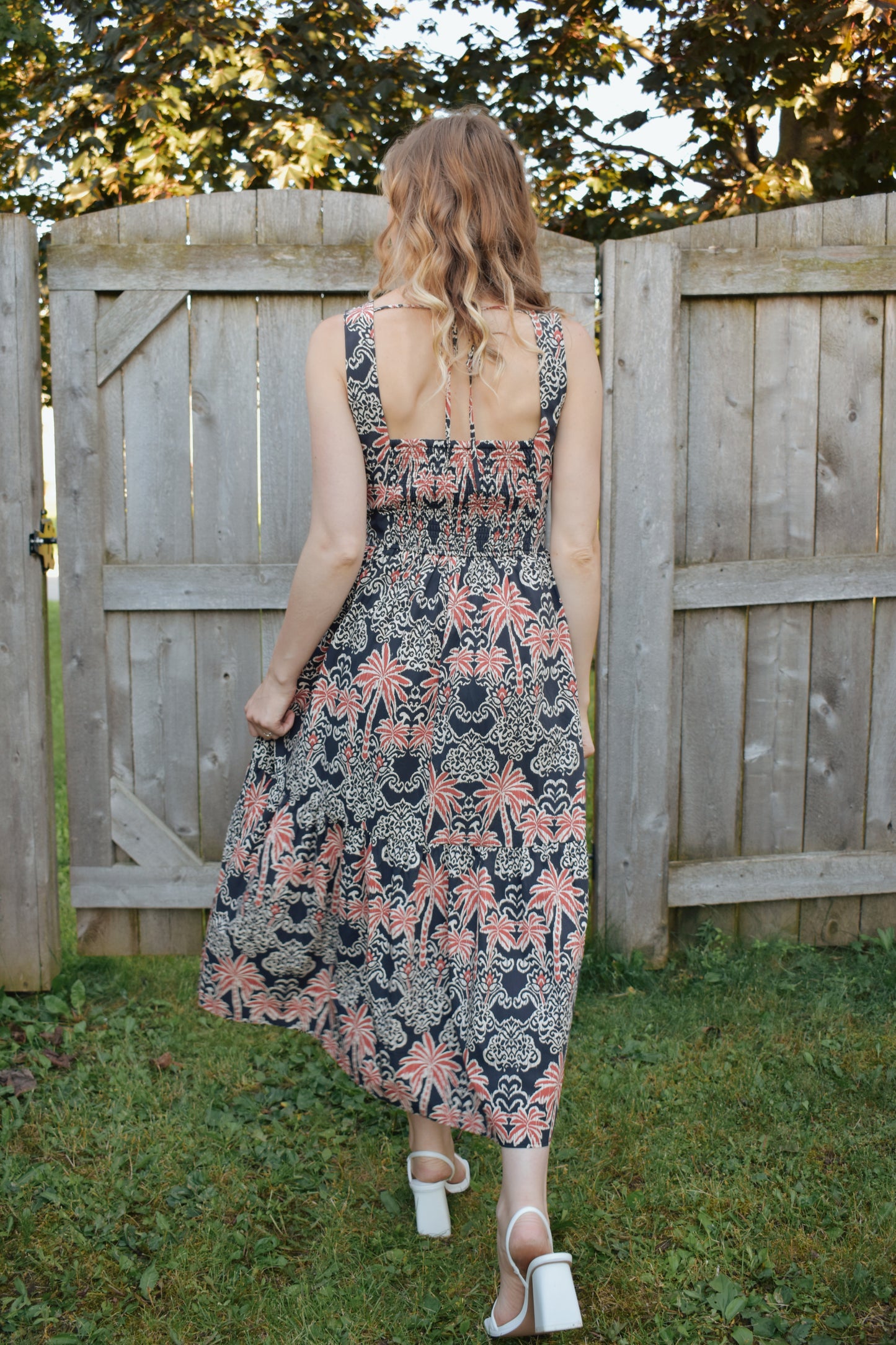 v neck midi dress with oval cut outs at waistline with circle loop in the center. square neck on back with tie across the top. sleeveless with thick tank straps. dark blue background with white and light red summer print. smocked on back waistline for stretch.