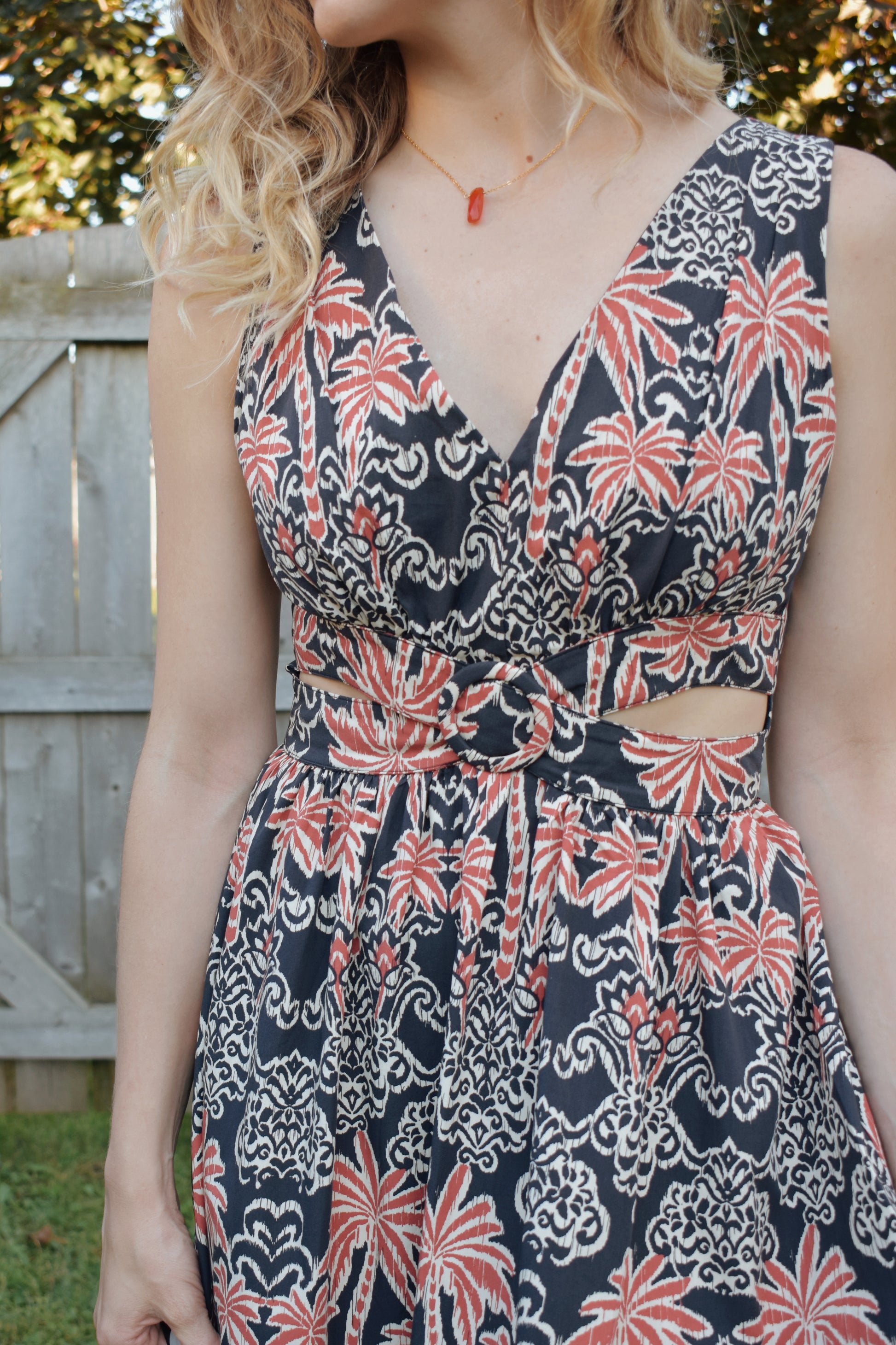 v neck midi dress with oval cut outs at waistline with circle loop in the center. square neck on back with tie across the top. sleeveless with thick tank straps. dark blue background with white and light red summer print. smocked on back waistline for stretch.