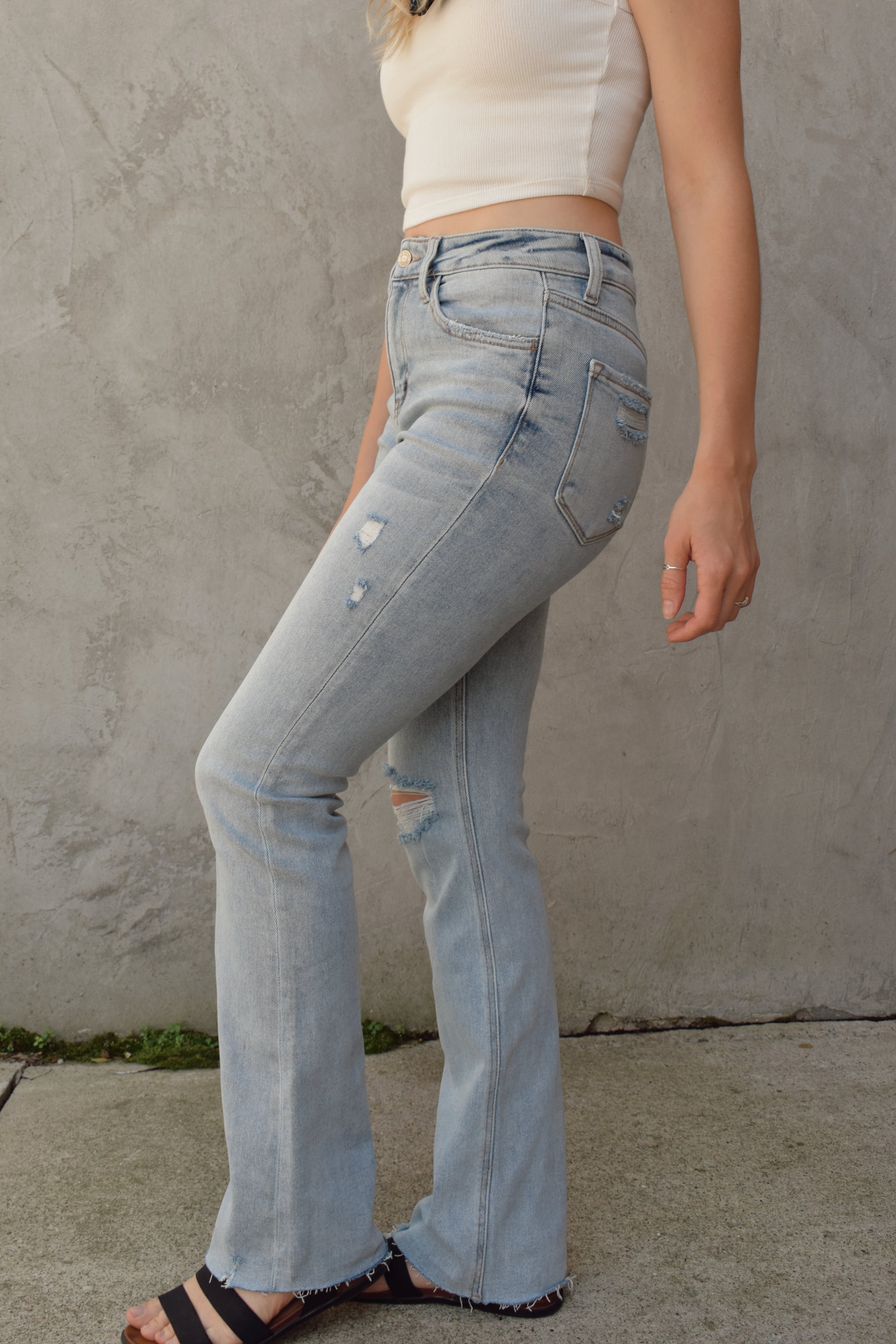 full length high rise bootcut jeans light wash with hole in right knee and slight distressing on other leg raw hem stretch denim  distressing on back pockets