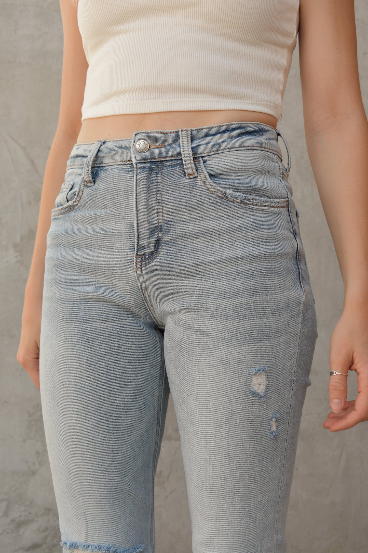 full length high rise bootcut jeans light wash with hole in right knee and slight distressing on other leg raw hem stretch denim  distressing on back pockets