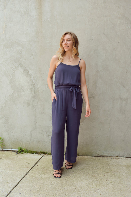 wide leg cami jumpsuit with fitted elastic waist band and tie. adjustable spaghetti straps. has side seam pockets. scoop neck and flowy lightweight fabric.