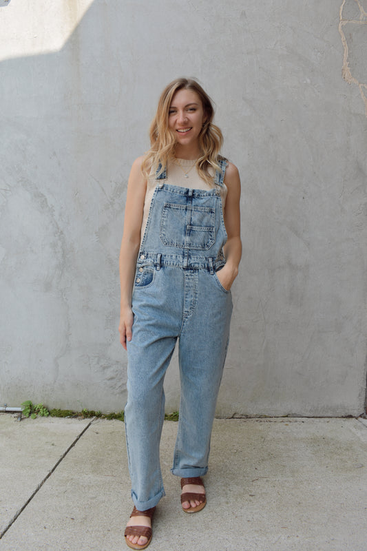 acid washed denim overalls with a relaxed leg and cuffed hem. square neckline with adjustable straps. pockets in front and back and the pouch pocket on the front is split into two with an added smaller pocket. has beltloops. no holes. 