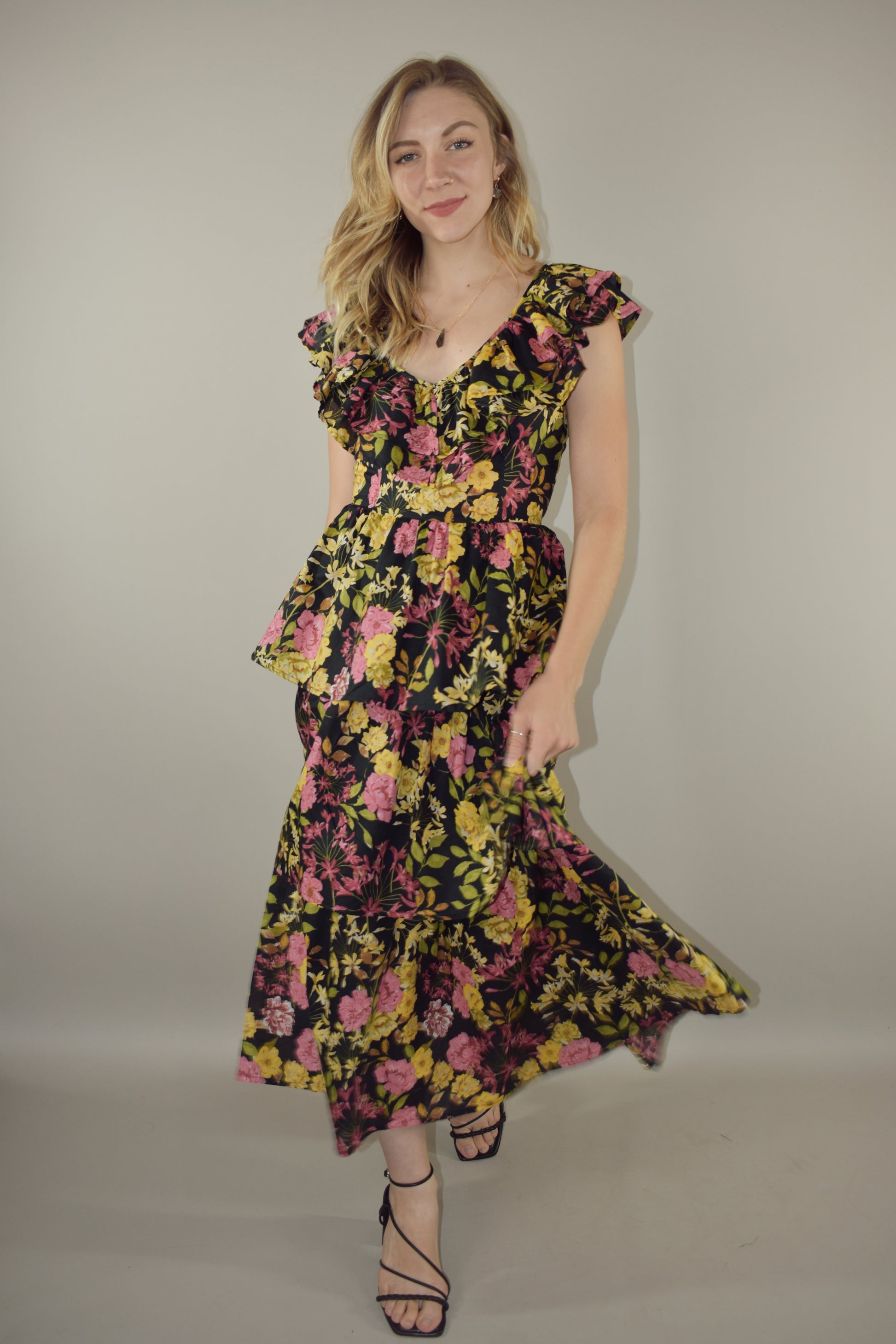 midi tiered floral dress with black background and pink, yellow, green and neutral tones in the floral pattern. v neck with cap flutter sleeves that are also layered. fitted bodice and invisible back zip enclosure. 