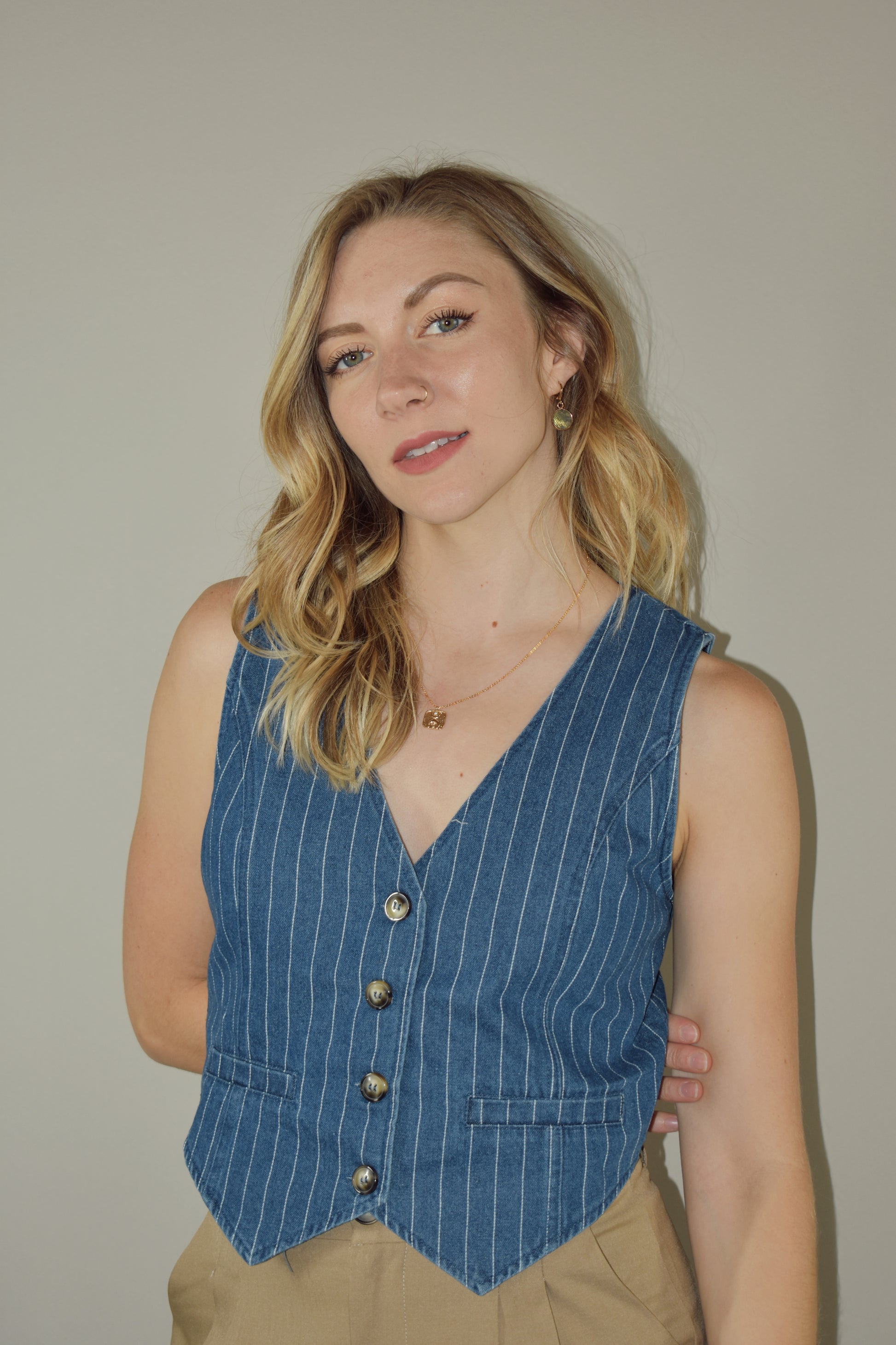 medium wash denim v neck button down vest with white vertical pin stripes. fake front tailored pockets.