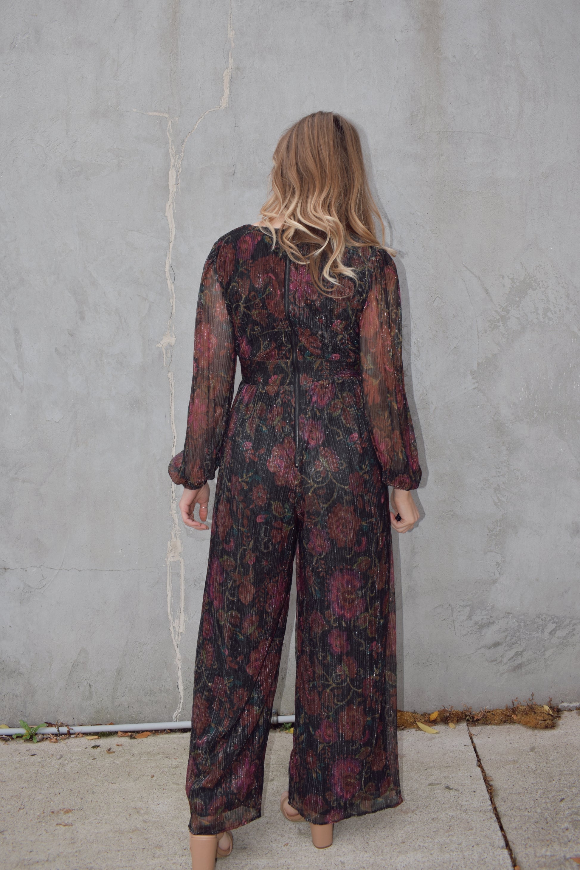 stunning wide leg jumpsuit with fitted bodice panel and deep v neck with circular metal piece at sternum. sheer long sleeves with elastic at cuffs. zip back enclosure