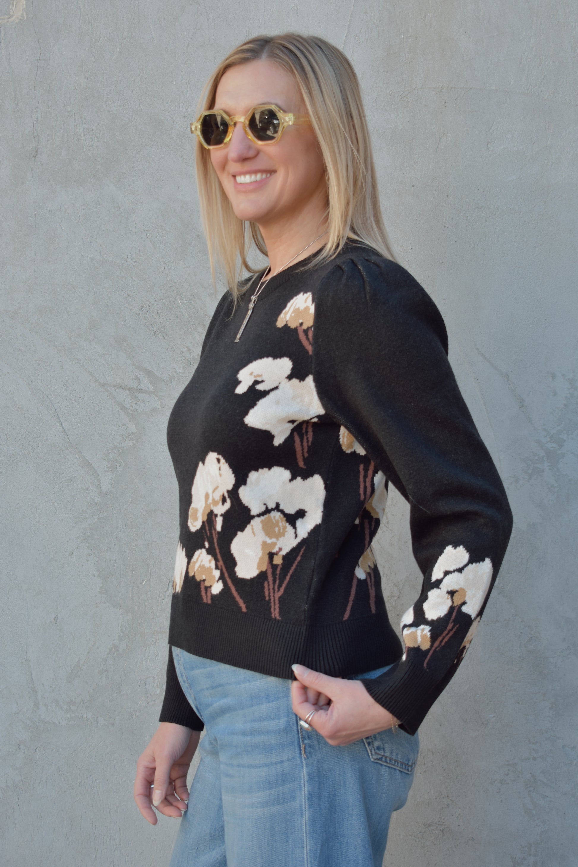 black sweater with cotton flower design on the left side and on lower part of the sleeve in cream and brown colors. slight balloon sleeve effect at shoulders. slightly cropped hem. round neck.