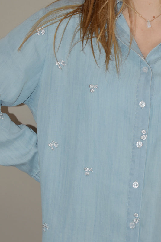 light denim colored chambray button down long sleeve shirt full length relaxed fit one breast patch pocket with small white embroidered flowers