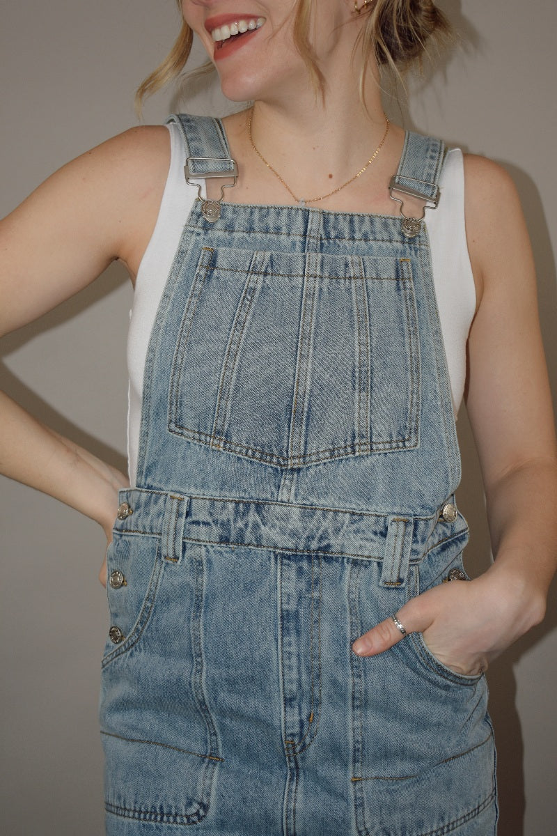 light wash denim overall midi skirt dress with front slit, square neckline on front and back, adjustable straps, has beltloops, deep front pockets, back pockets, button enclosure on both sides