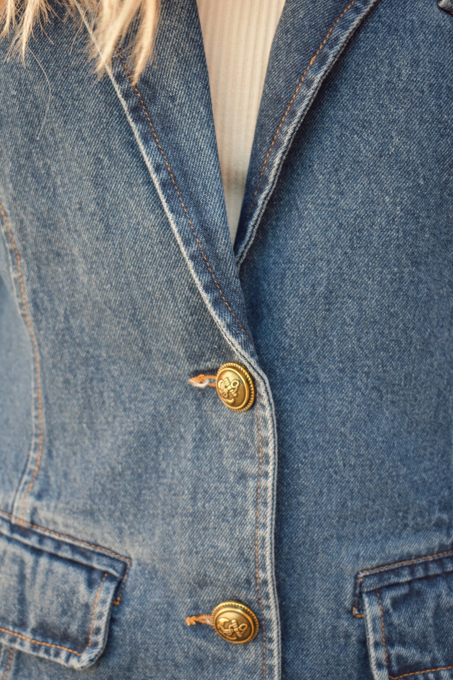 dark wash denim blazer with two gold buttons with an anchor design on them.  pockets with flaps on top, one breast pocket, fitted. full length. slit on back middle hem