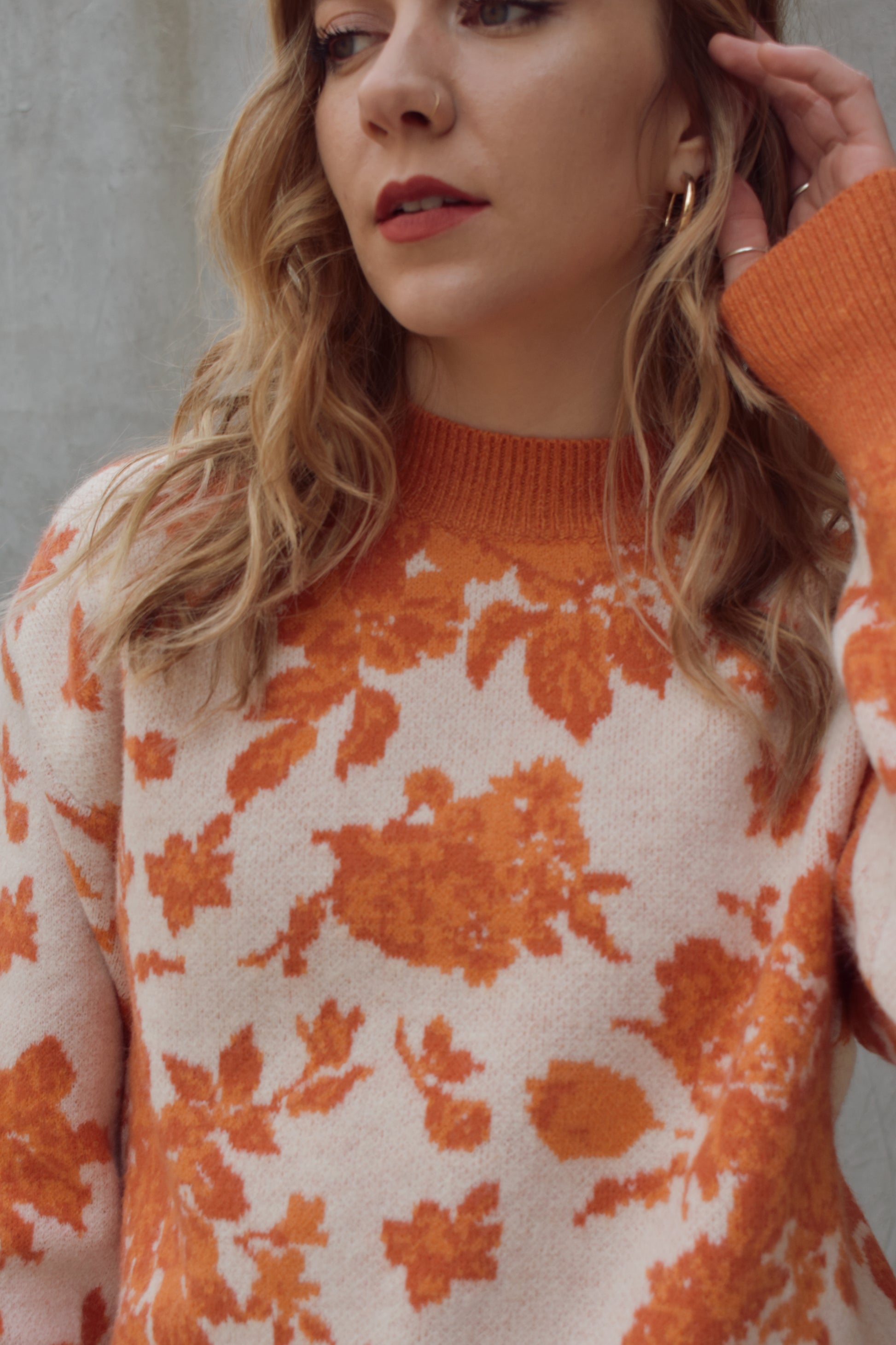 ivory and shades of orange high neck sweater with a leafy floral design. hemline neckline and cuffs are solid orange and ribbed. full length, relaxed fit, drop shoulder.