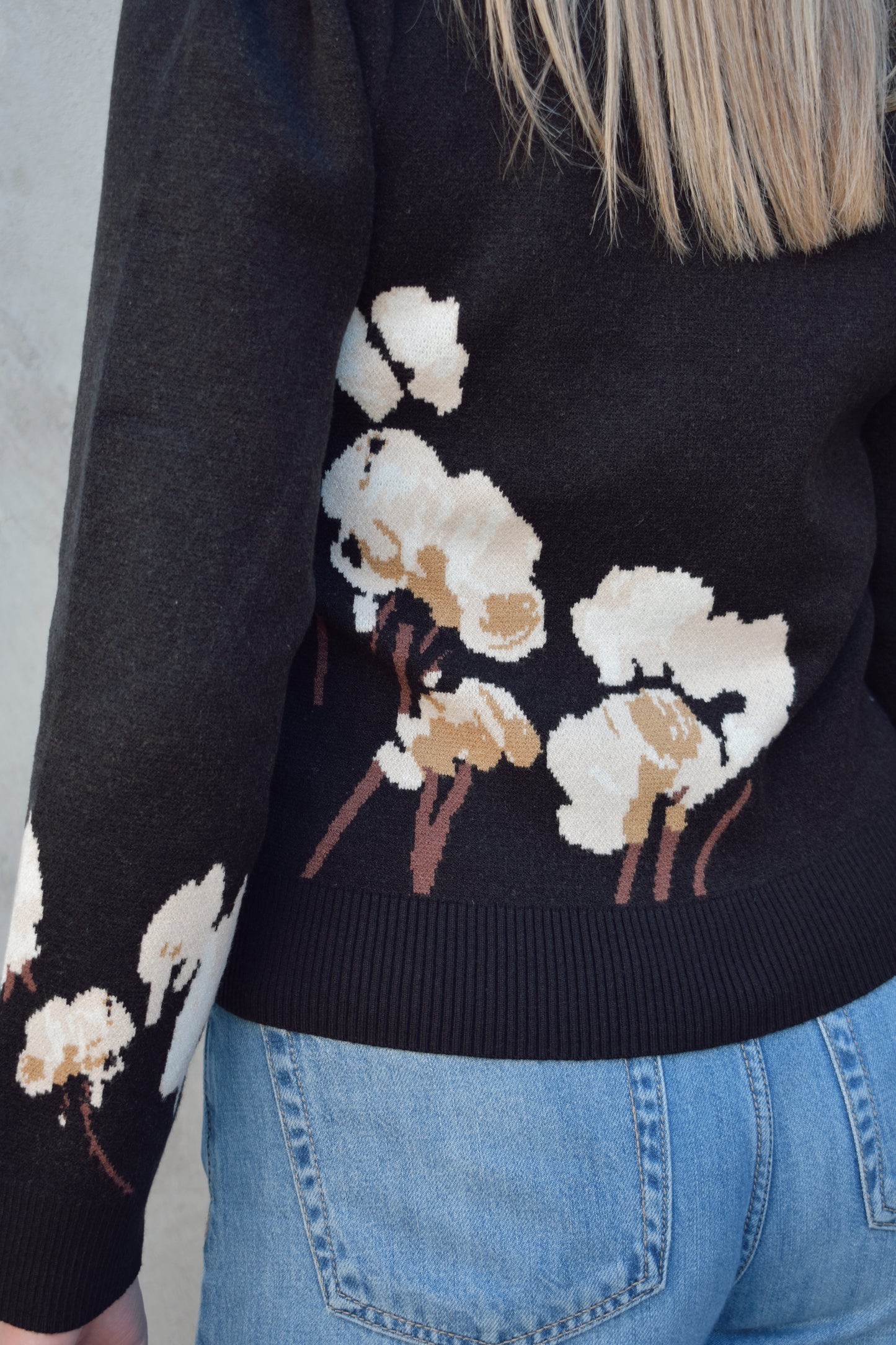 black sweater with cotton flower design on the left side and on lower part of the sleeve in cream and brown colors. slight balloon sleeve effect at shoulders. slightly cropped hem. round neck.