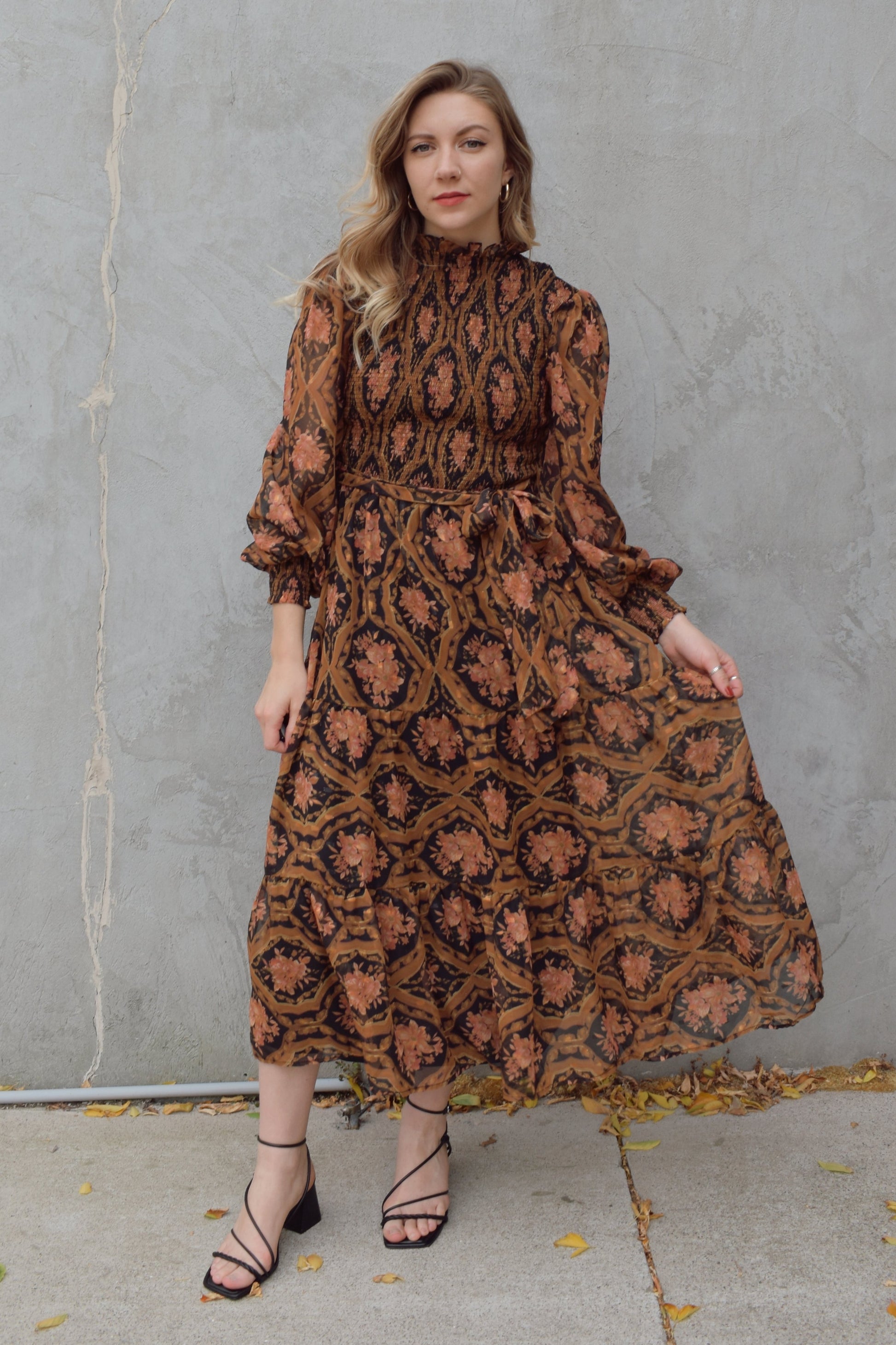 long sleeve high/mock neck midi dress with smocked bodice and cuffs, sheer sleeves, flowy skirt, fabric tie at waist, floral boho tapestry pattern. double button at back of neck