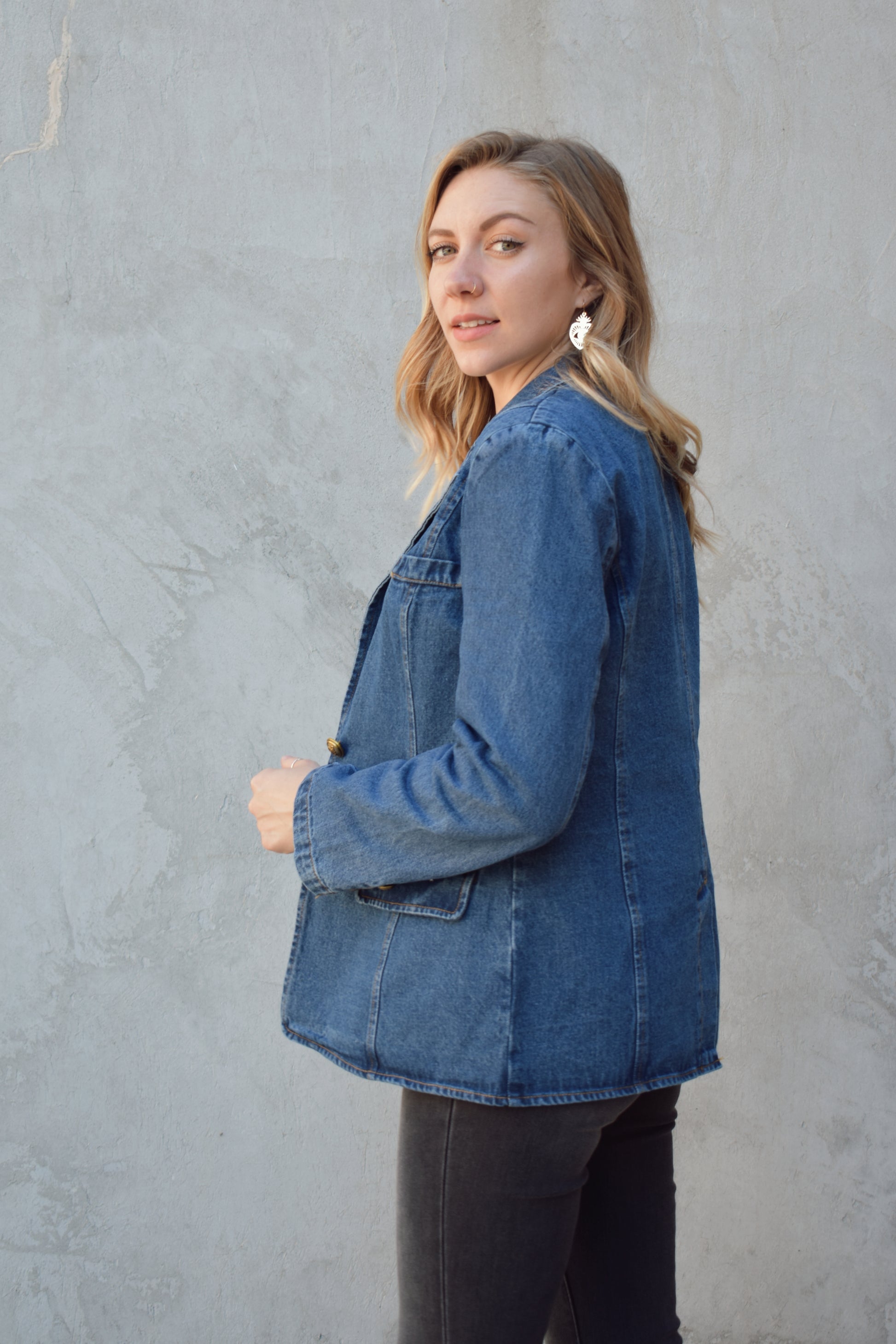 dark wash denim blazer with two gold buttons with an anchor design on them.  pockets with flaps on top, one breast pocket, fitted. full length. slit on back middle hem