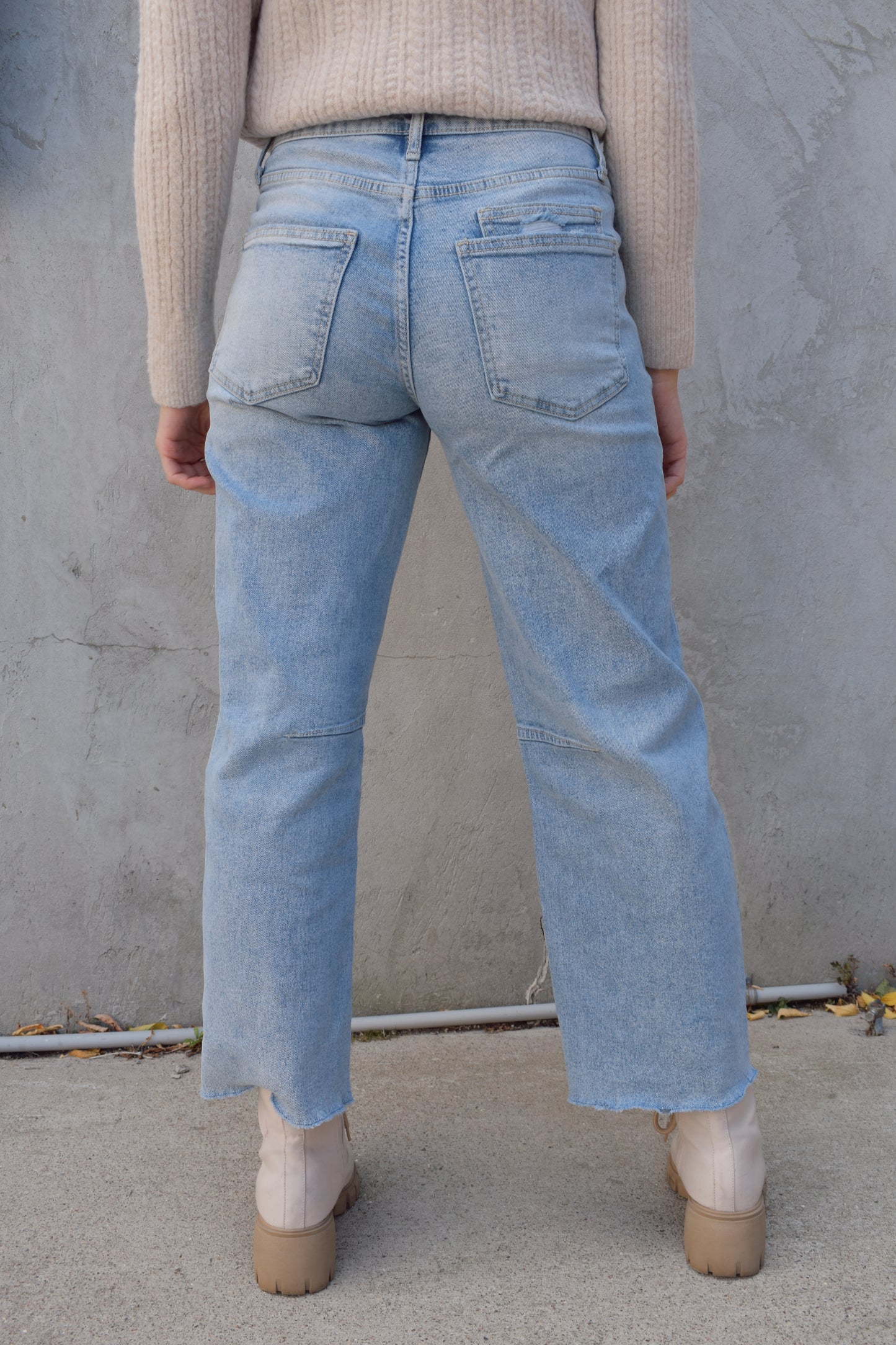 high rise barrel jeans, light wash, stretch denim, no holes, patch pockets in front, back pocket on right has a double pocket detail, zip and button enclosure, has belt loops, raw hem cropped, edgy seam detail at knee