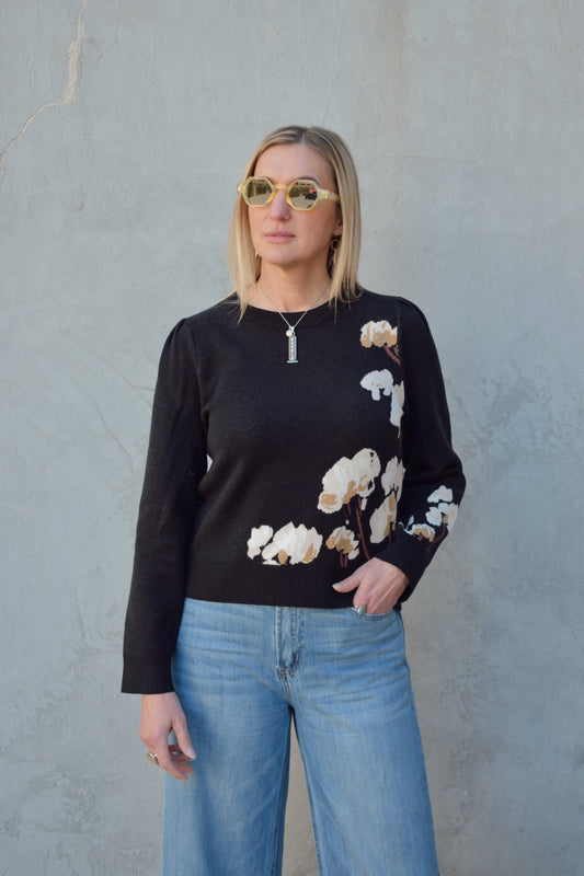 black sweater with cotton flower design on the left side and on lower part of the sleeve in cream and brown colors. slight balloon sleeve effect at shoulders. slightly cropped hem. round neck.