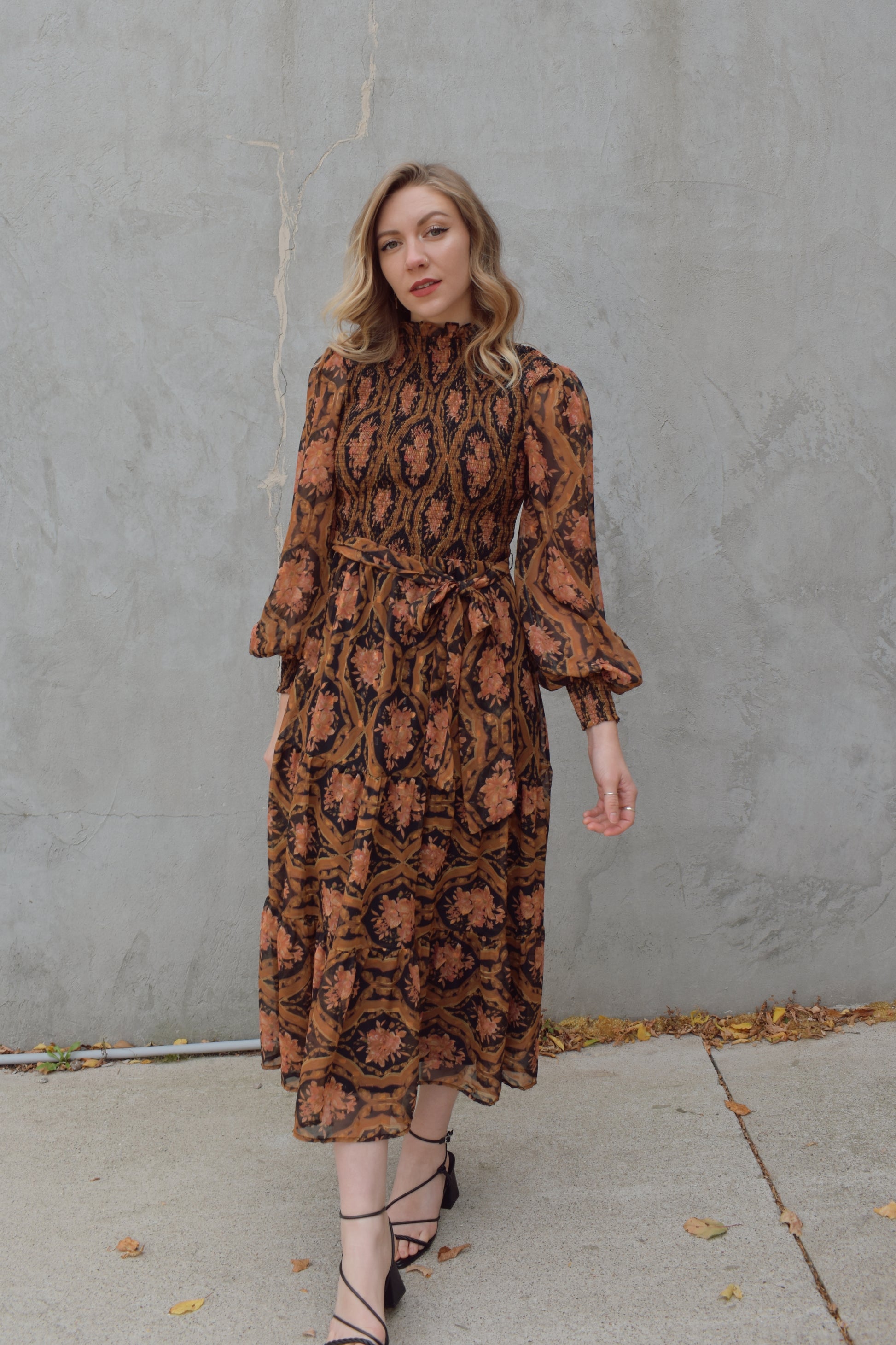 long sleeve high/mock neck midi dress with smocked bodice and cuffs, sheer sleeves, flowy skirt, fabric tie at waist, floral boho tapestry pattern. double button at back of neck