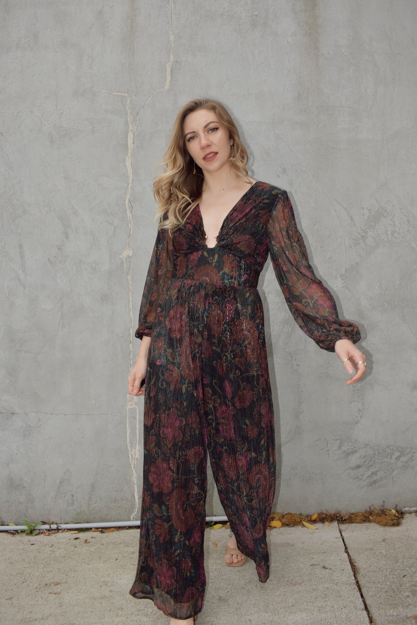 stunning wide leg jumpsuit with fitted bodice panel and deep v neck with circular metal piece at sternum. sheer long sleeves with elastic at cuffs. zip back enclosure