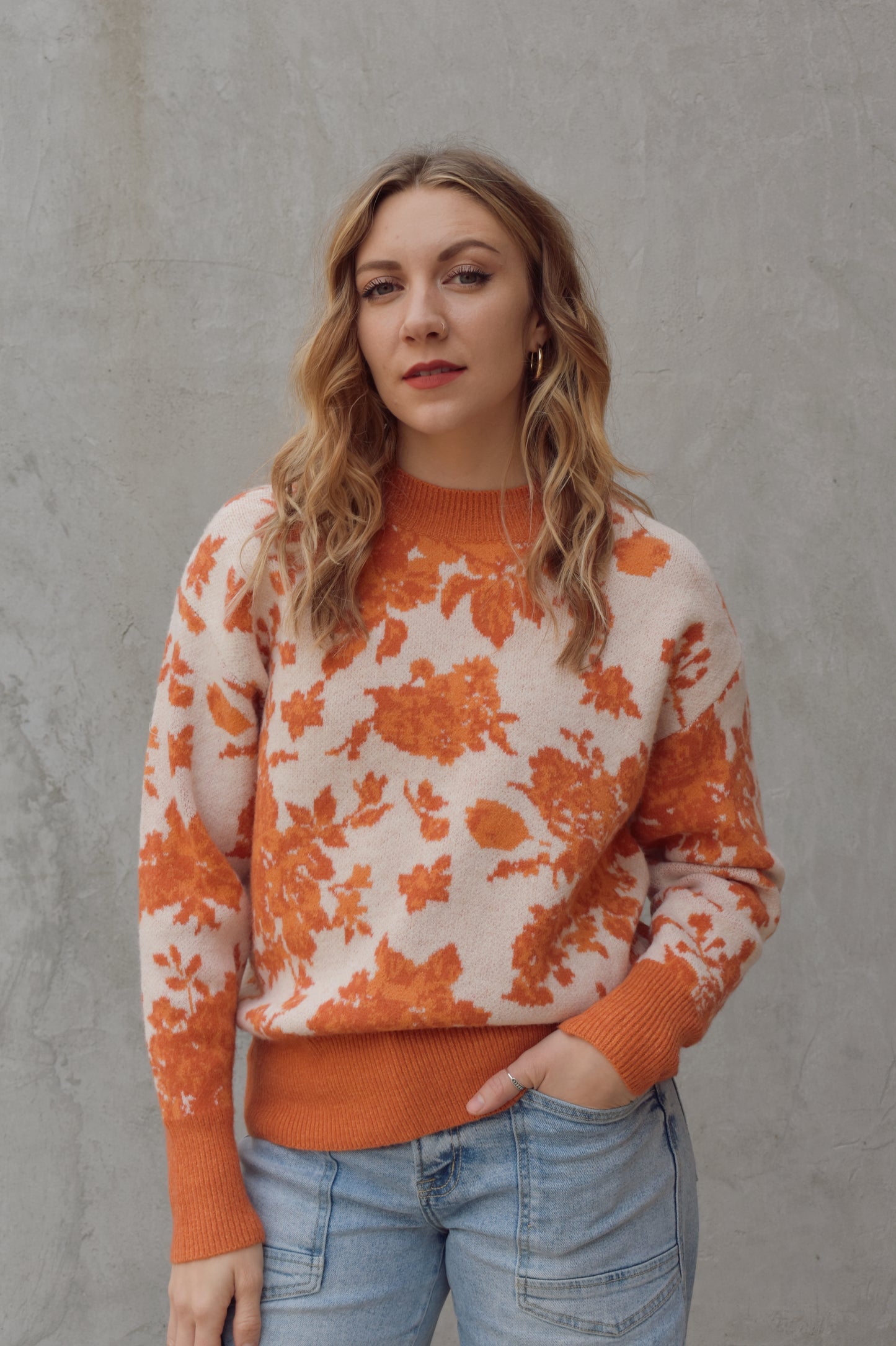 ivory and shades of orange high neck sweater with a leafy floral design. hemline neckline and cuffs are solid orange and ribbed. full length, relaxed fit, drop shoulder.