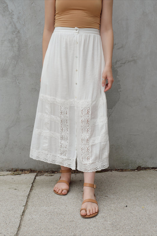 white maxi skirt with lace trim detailing that goes about half way up the skirt on the front and has buttons down the whole front. Has pockets and is lined. elastic on back of waistband