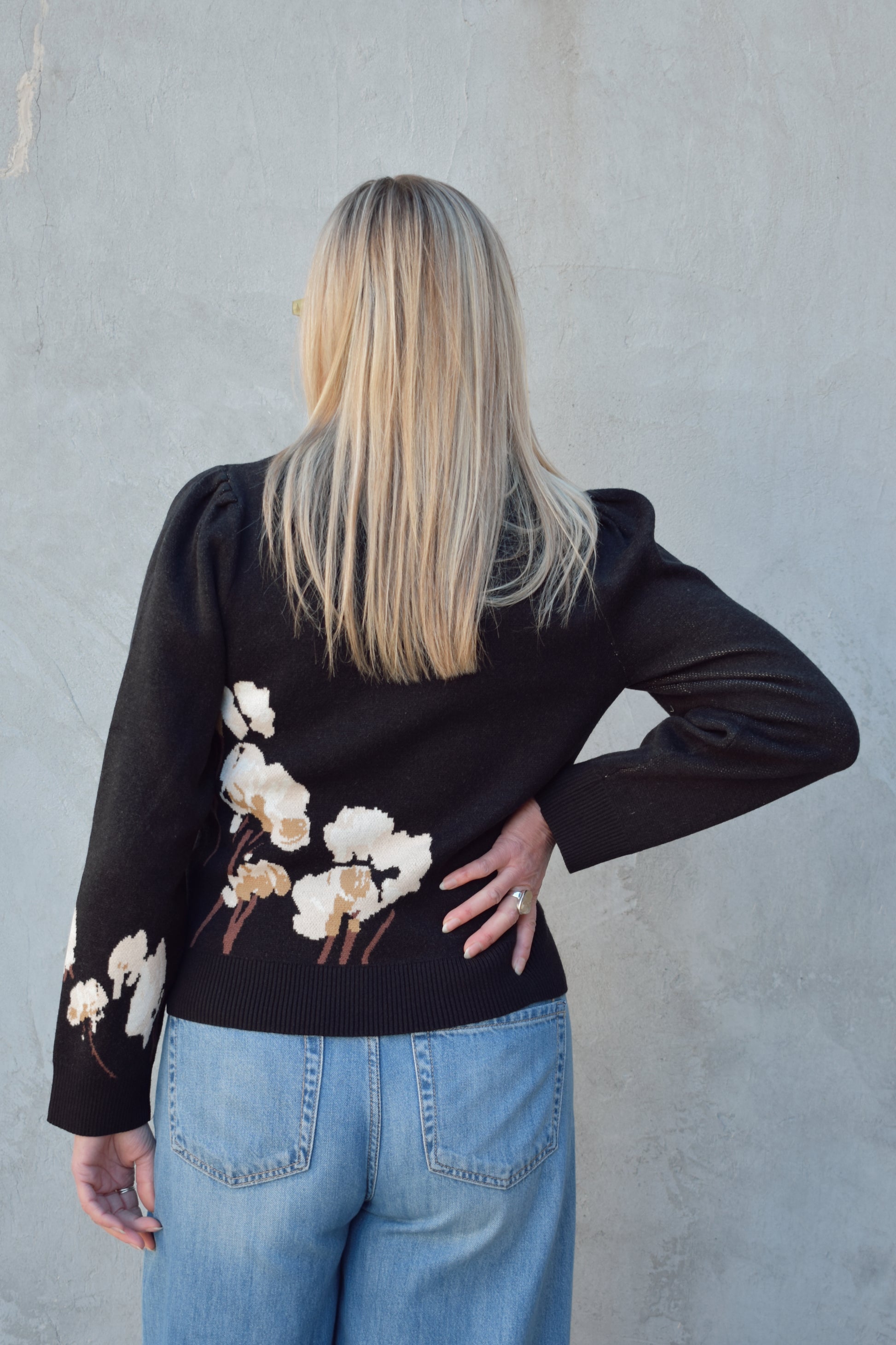 black sweater with cotton flower design on the left side and on lower part of the sleeve in cream and brown colors. slight balloon sleeve effect at shoulders. slightly cropped hem. round neck.