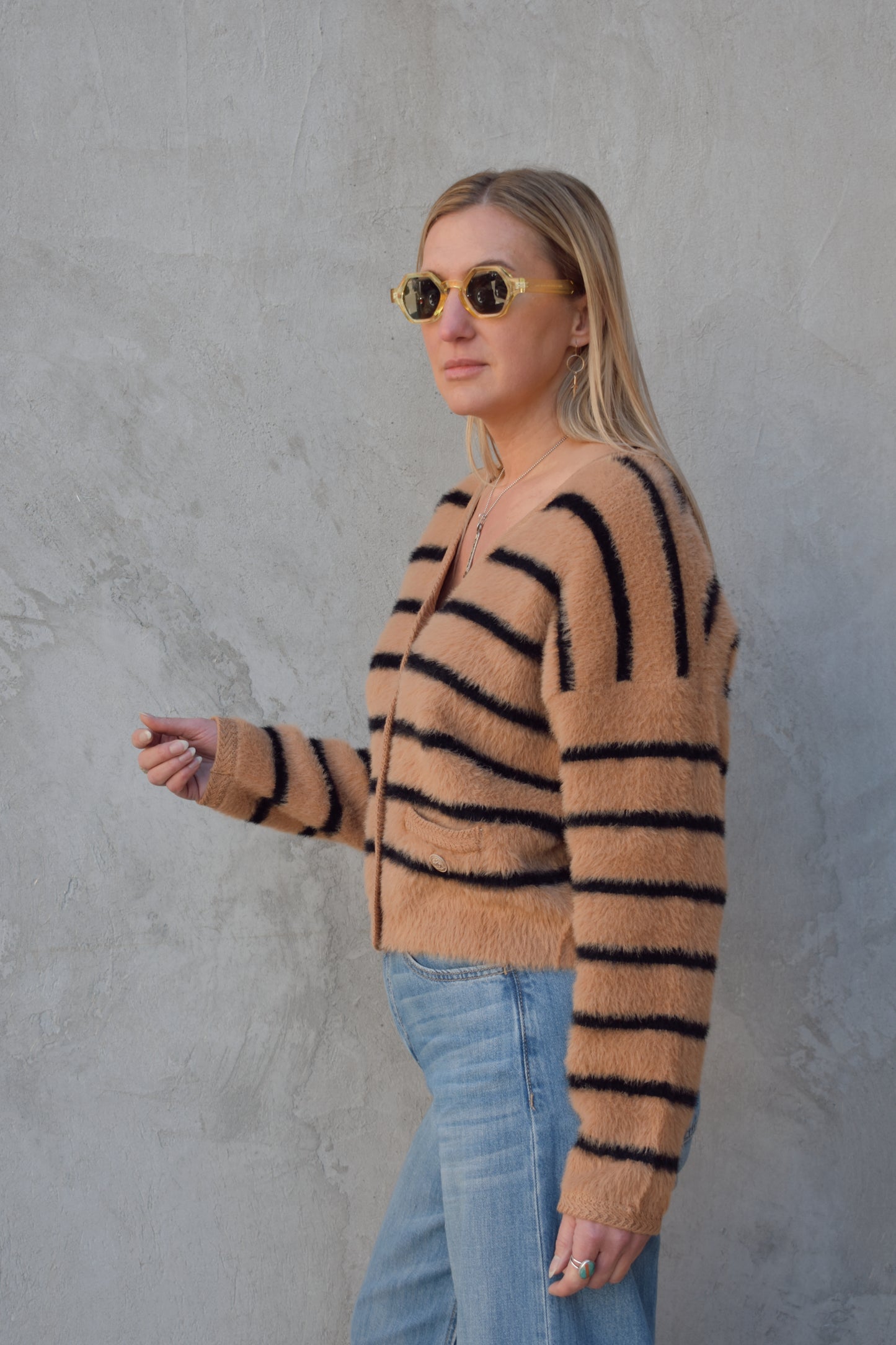 light brown mohair v neck button down cardigan with light brown sailor buttons and black horizontal stripes. two pockets on front that open at the top. outlined with a braided texture on neck line and down the front and on edge of pockets. drop shoulders, slightly cropped.